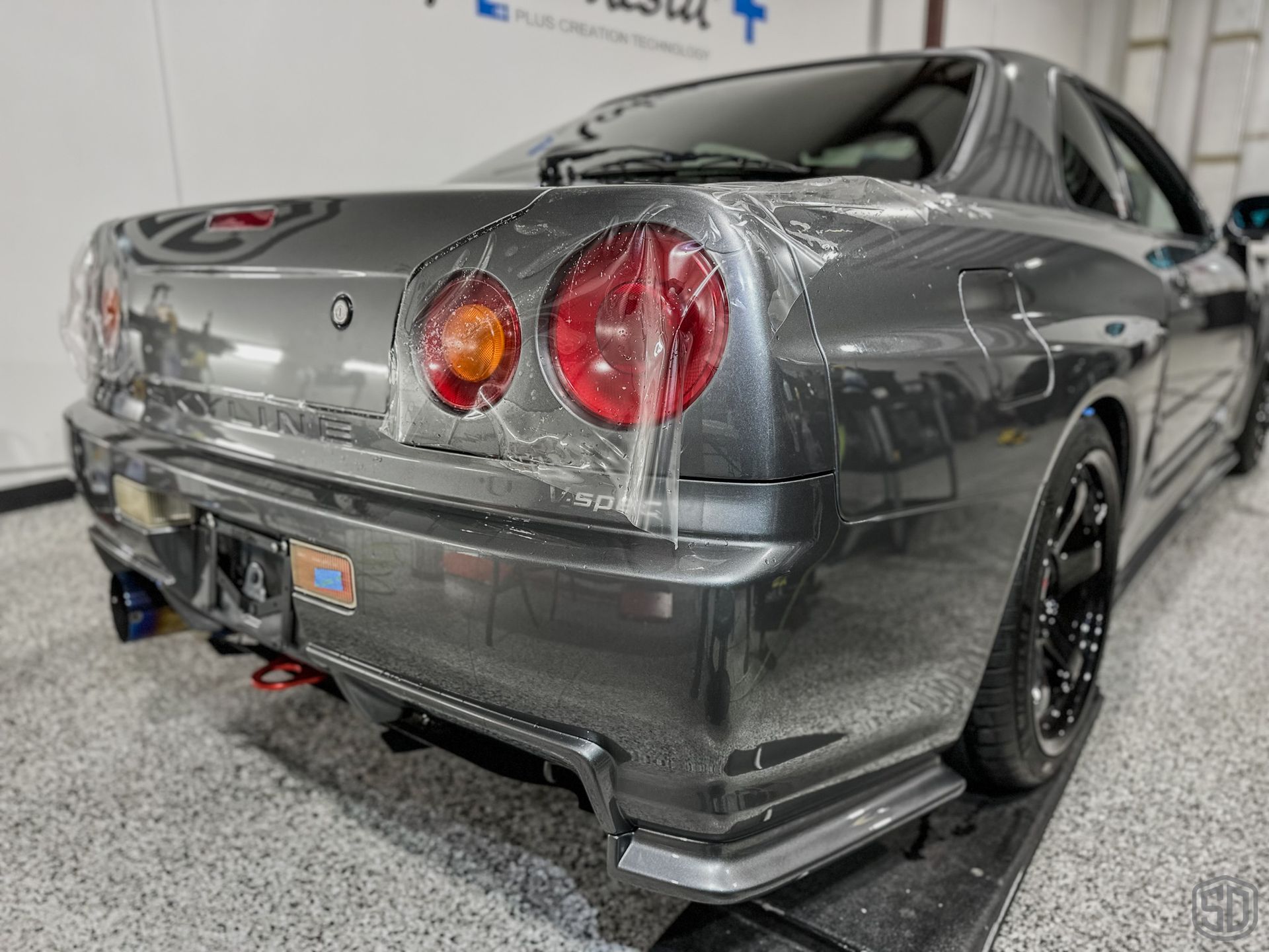 The rear end of a nissan skyline r34 is wrapped in plastic.