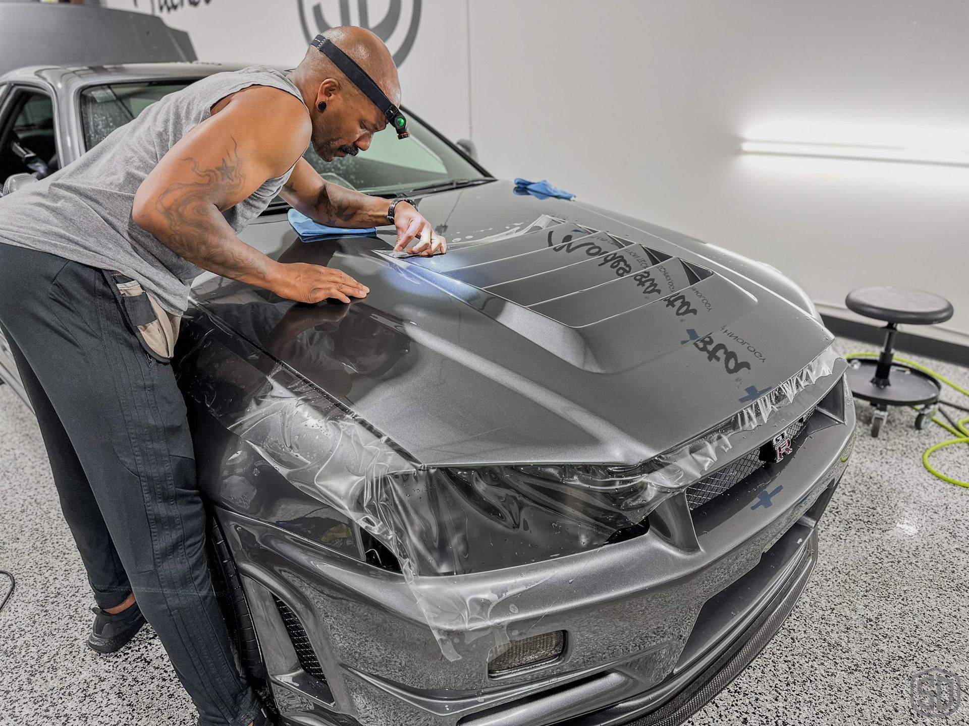 A man is wrapping a car in plastic in a garage.