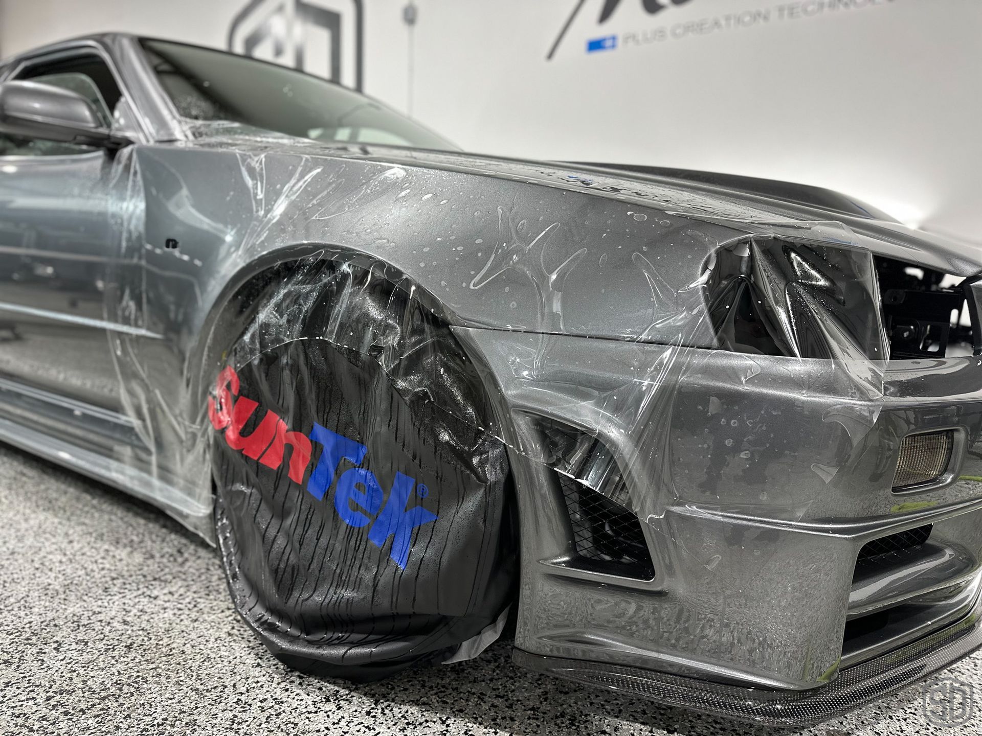 A close up of a car wrapped in plastic in a garage.