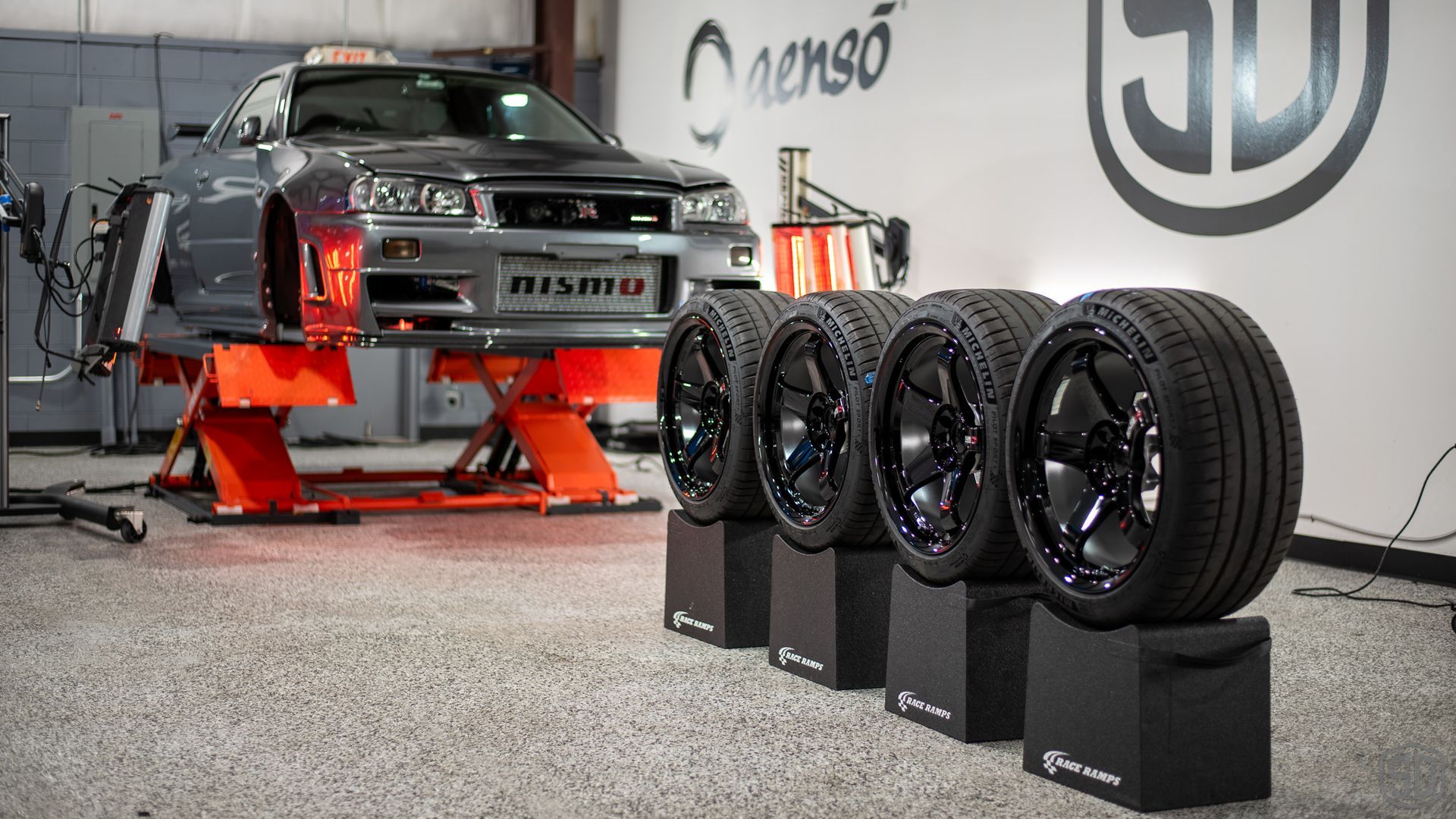 A car is sitting on a lift in a garage next to a row of tires.