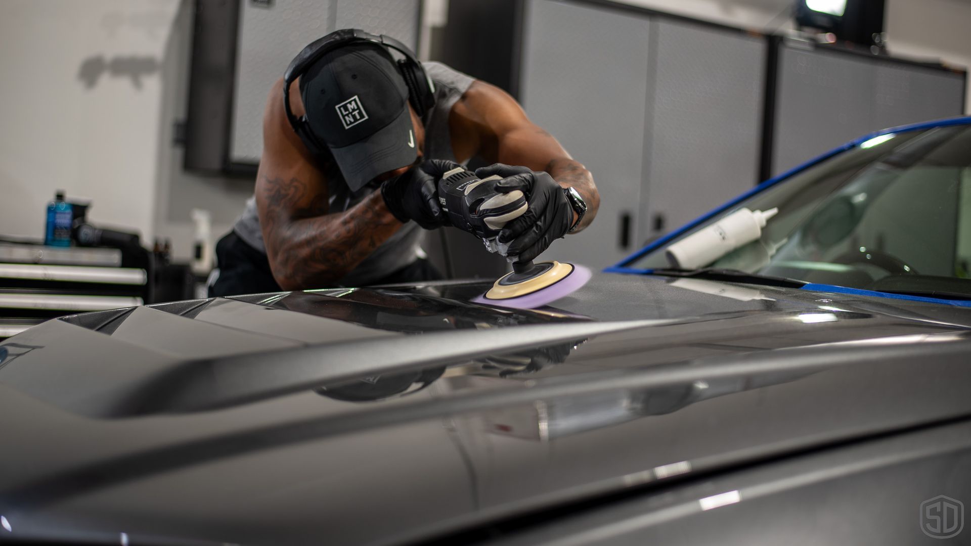 A man is polishing the hood of a car in a garage.
