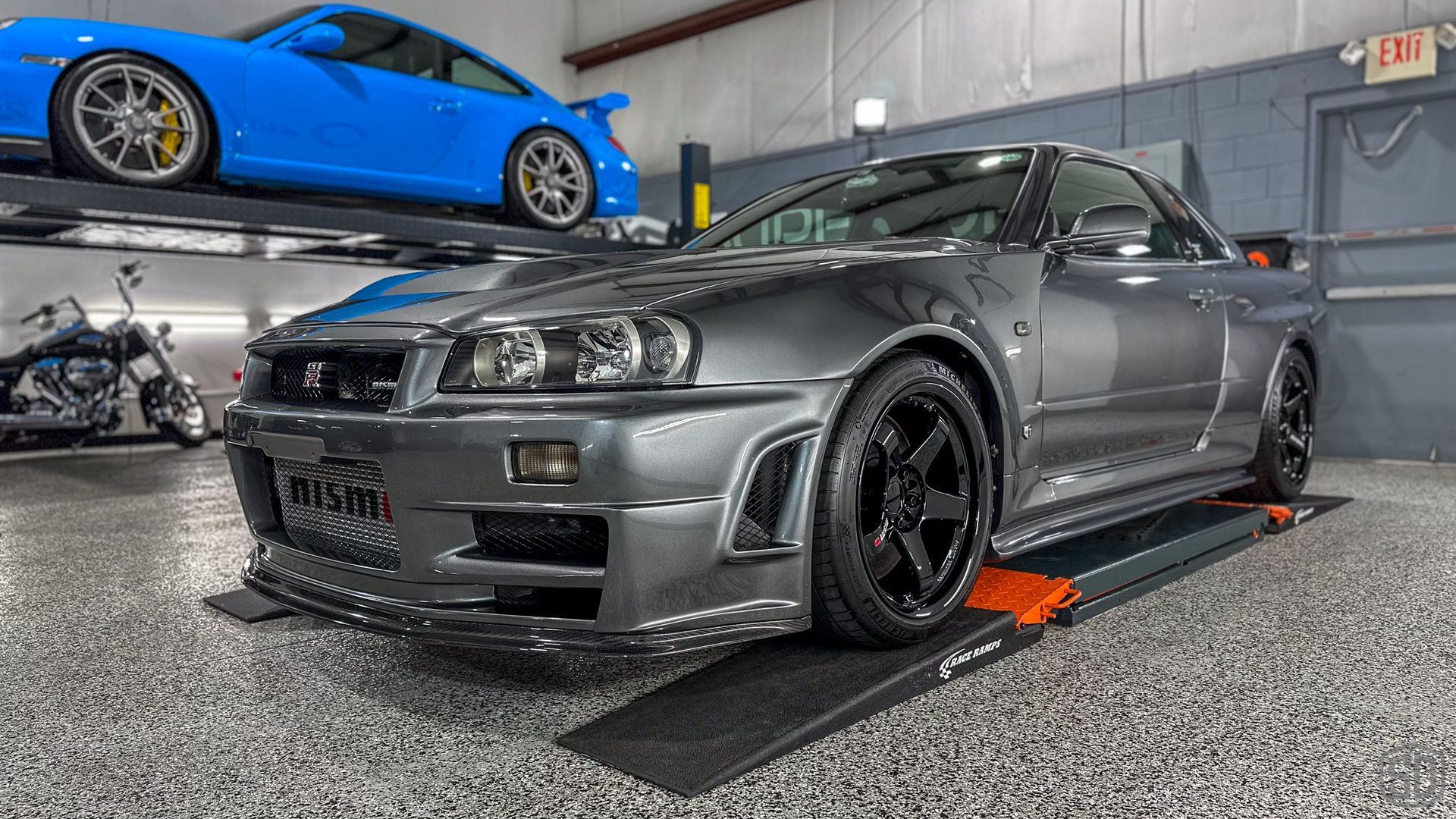 A gray sports car is parked in a garage next to a blue sports car.