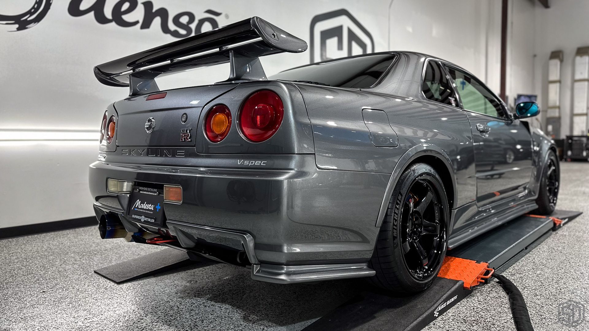 A gray sports car is parked on a ramp in a garage.