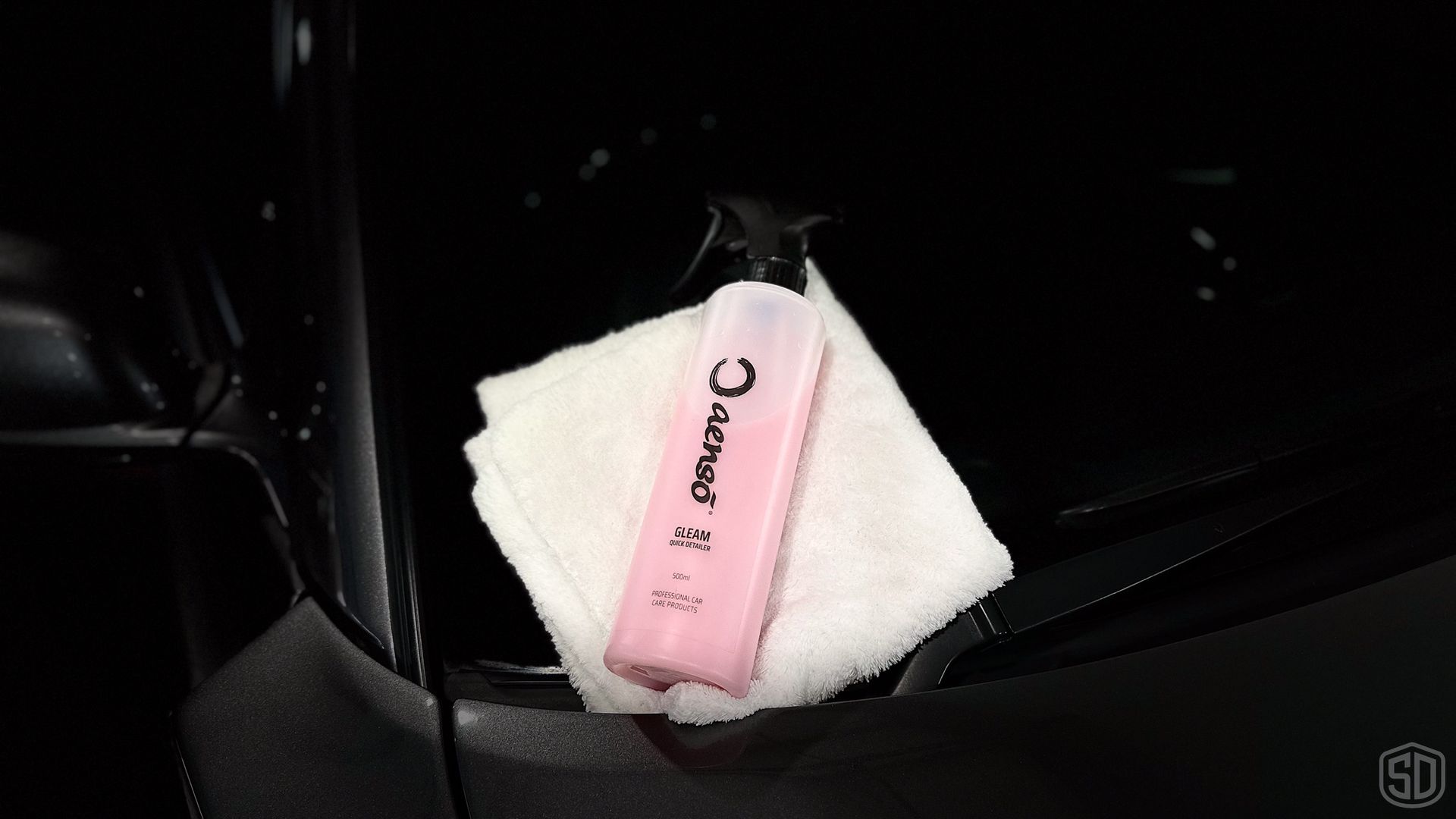 A pink bottle is sitting on a white towel on the side of a car.