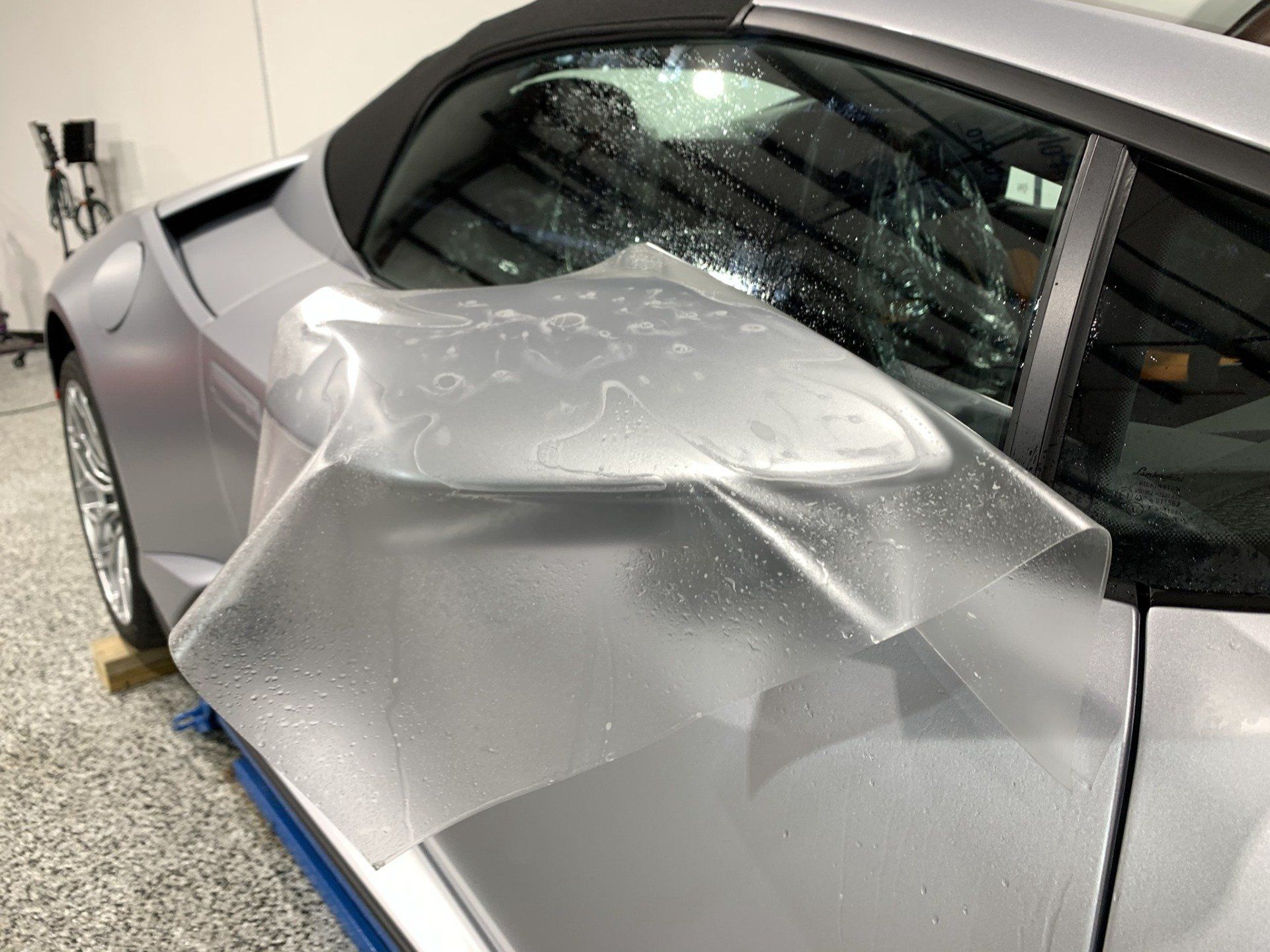 A silver sports car is wrapped in a clear plastic covering.