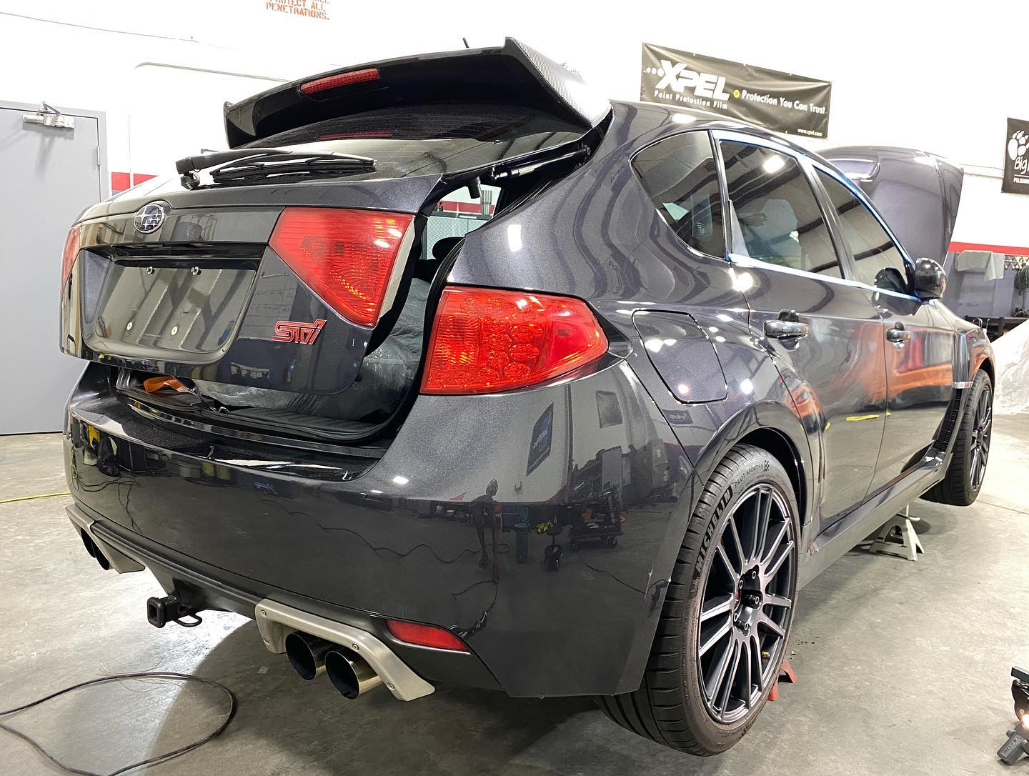 A black subaru wrx sti is parked in a garage with the hood up.