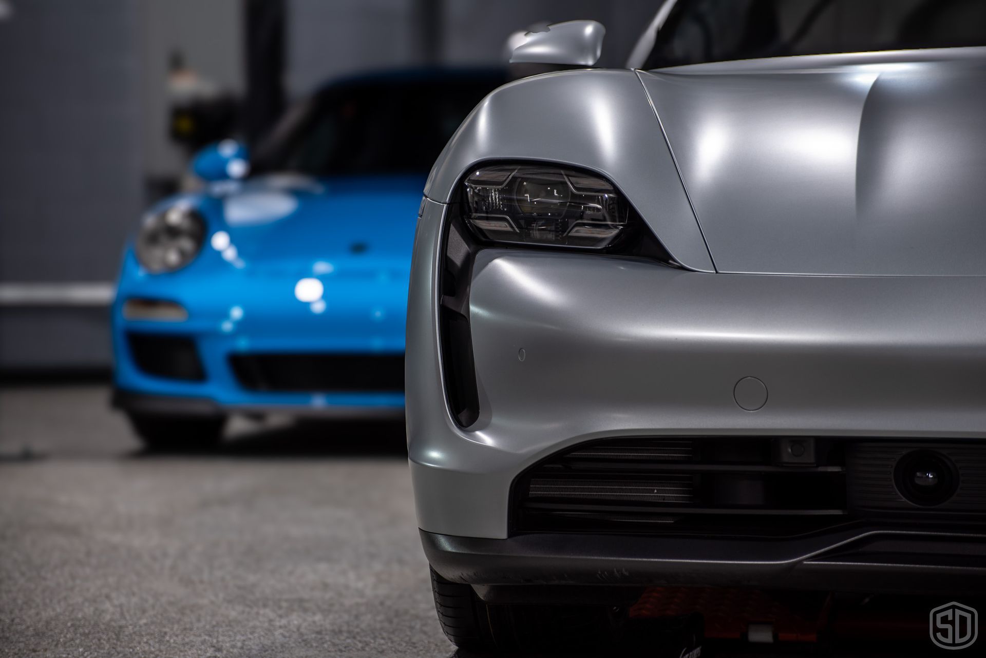A silver porsche taycan is parked next to a blue porsche 911 gt3 rs.