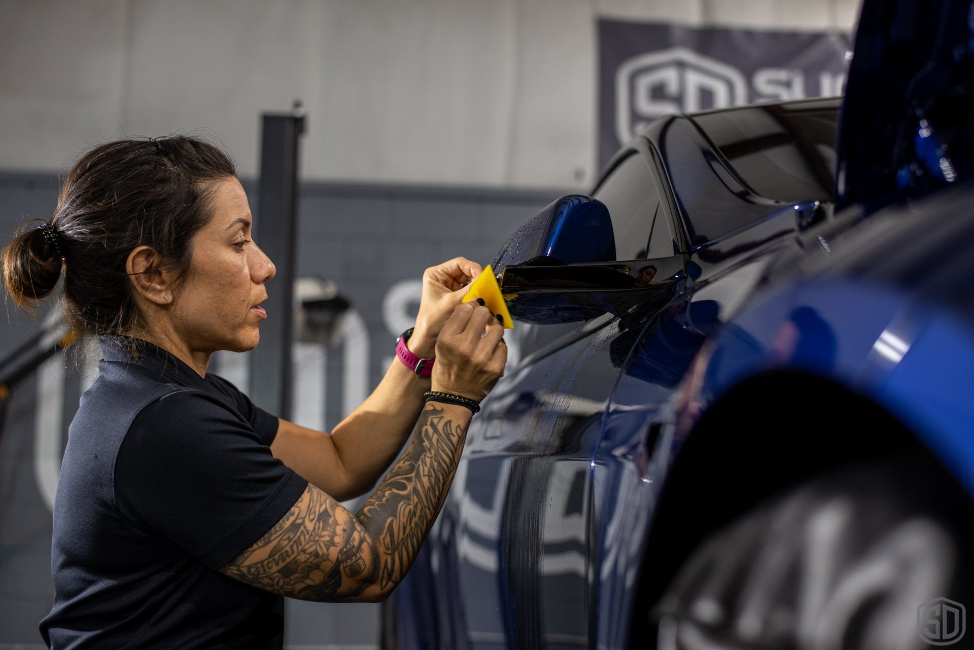 A woman is wrapping a blue car with a yellow tape.