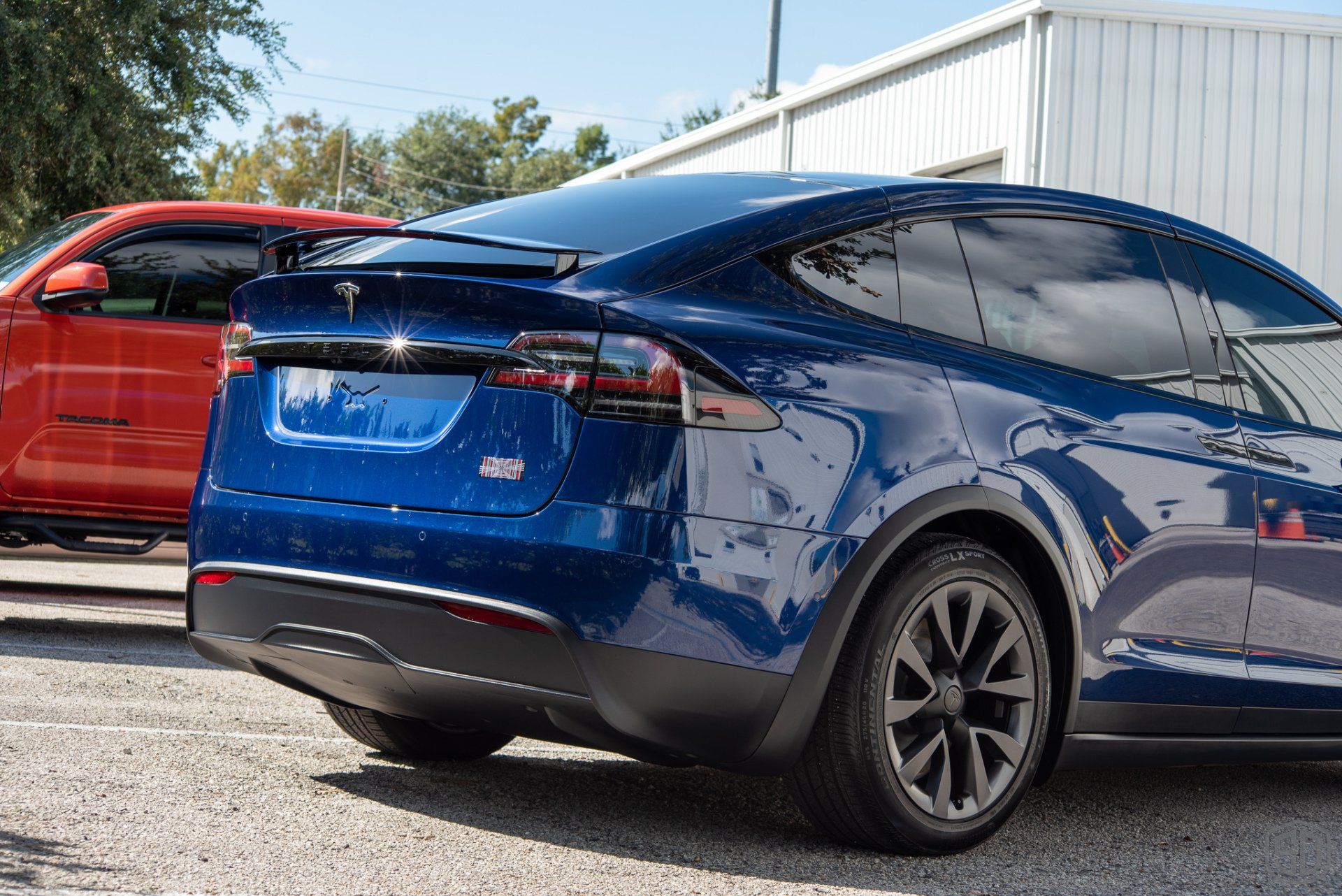 A blue tesla model x is parked next to a red tesla model s in a parking lot.