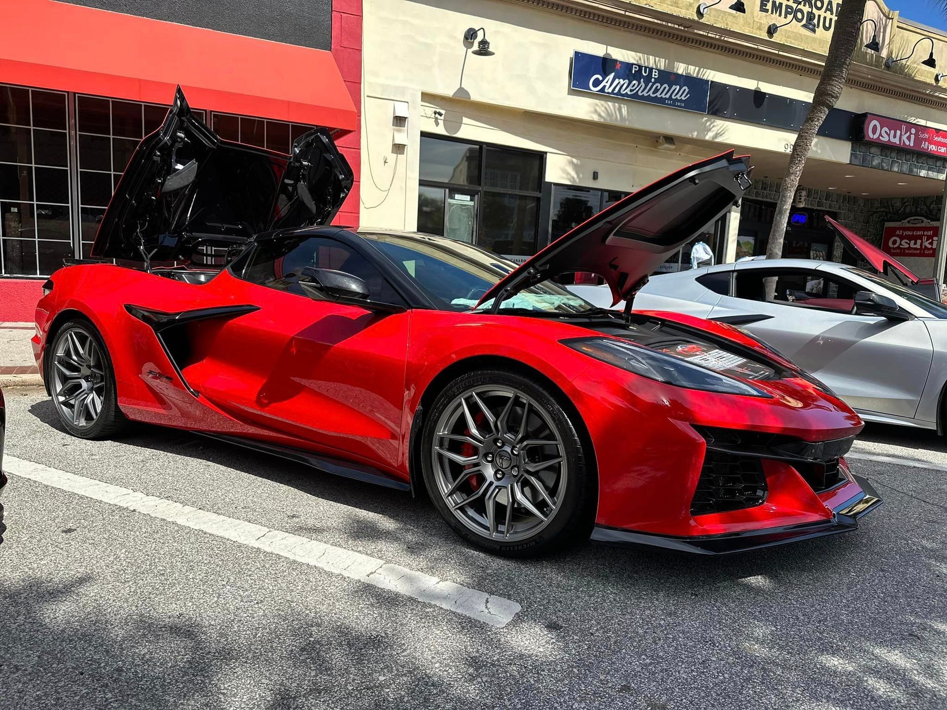 A red sports car with the hood up is parked in front of a building.