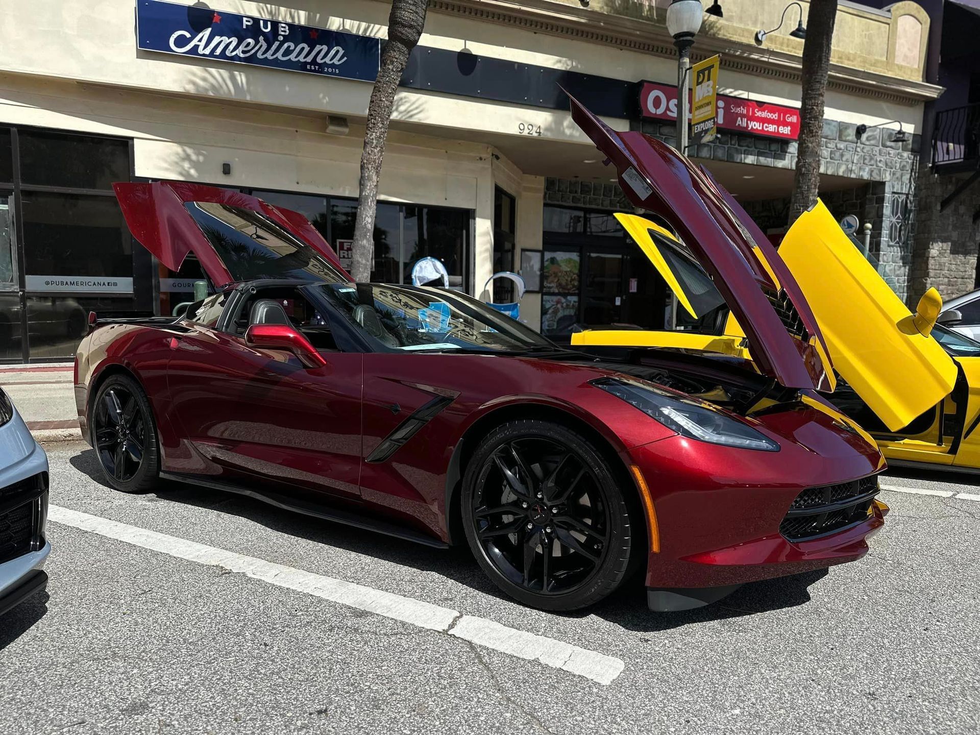 A red corvette is parked on the side of the road with its hood up.