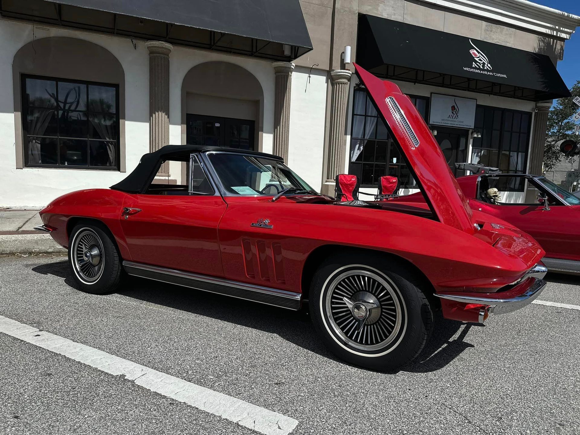 A red car with the hood up is parked in front of a building.
