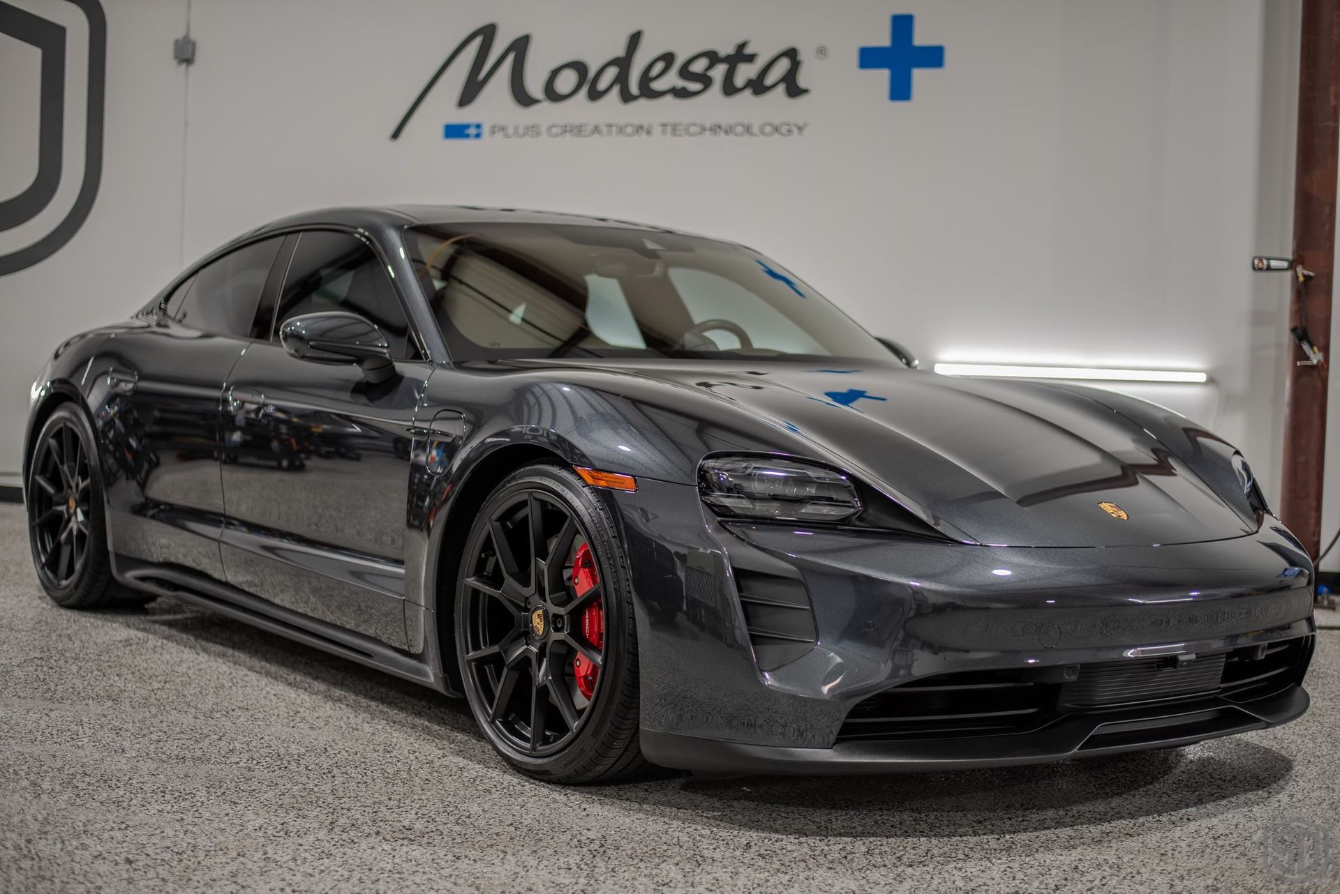 A black porsche taycan is parked in a garage.