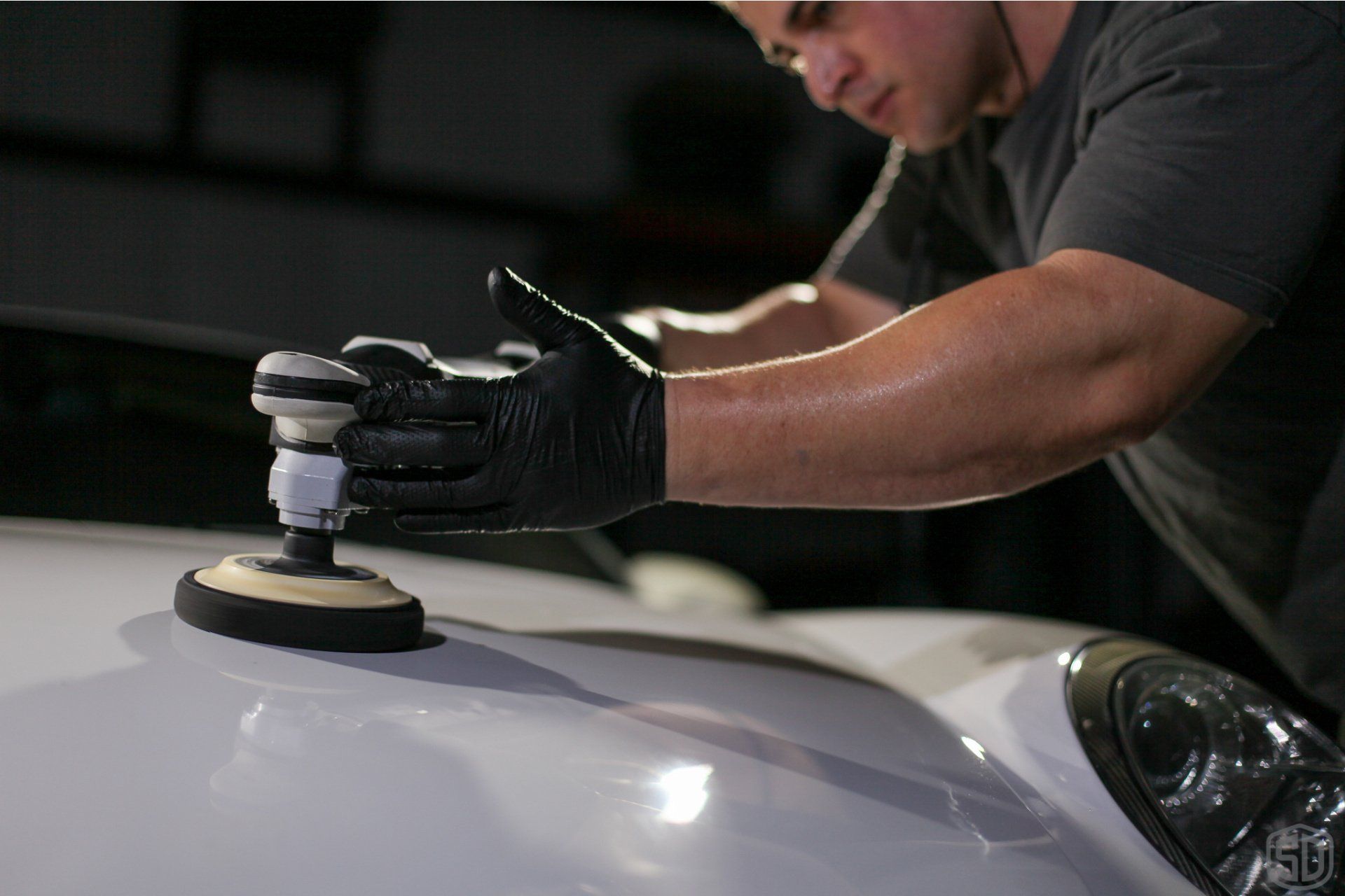 A man is polishing the hood of a white car.