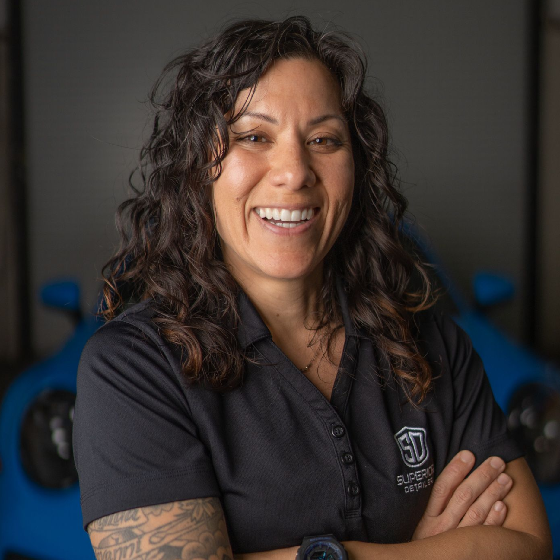 A woman in a black shirt is smiling in front of a blue car.