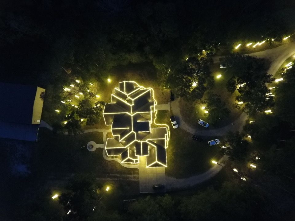 Overhead night view of a house and surrounding trees lit with warm white Christmas lights.
