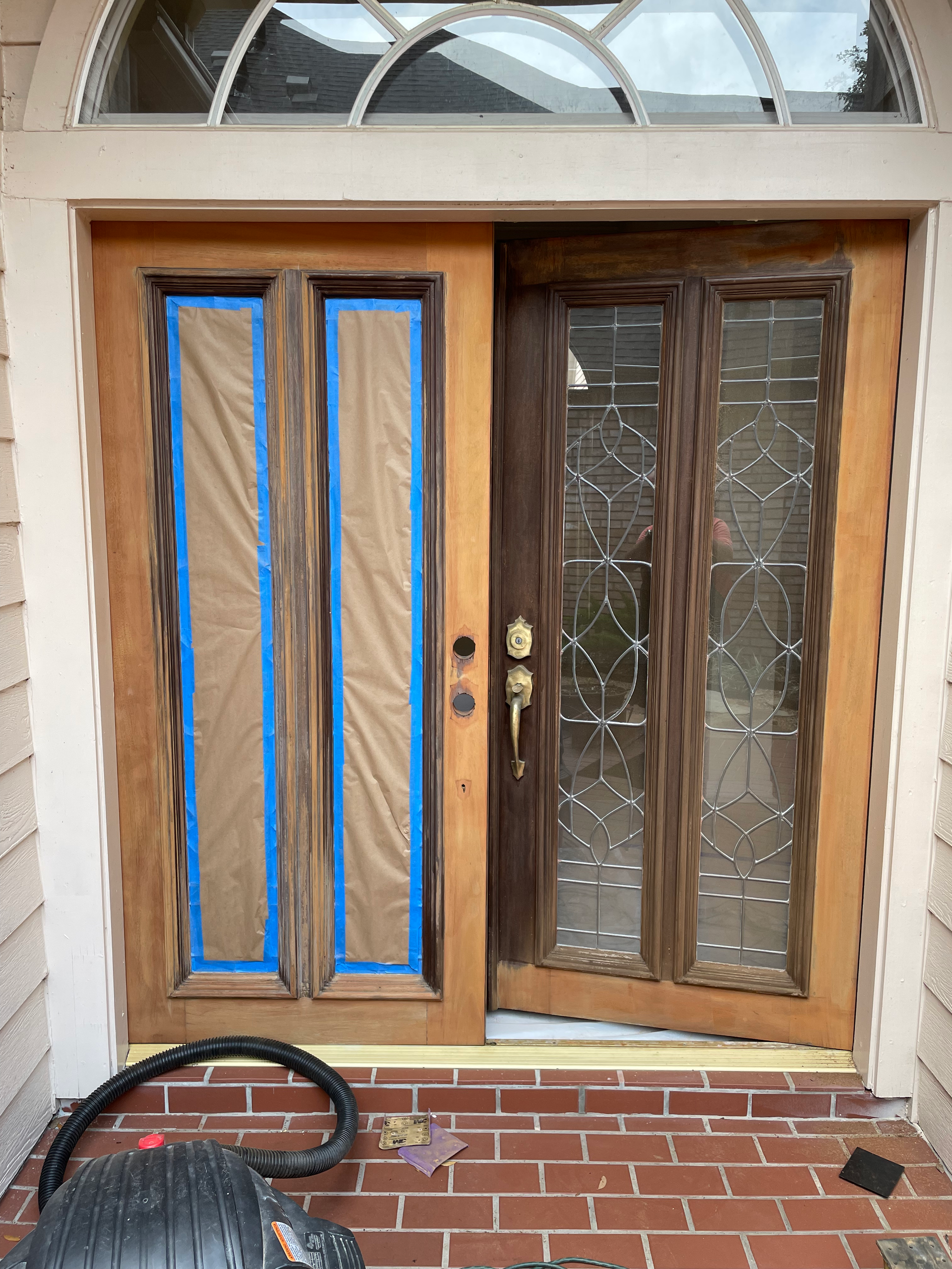 Exterior wooden door with stained right panel, taped left panel, and brick step.