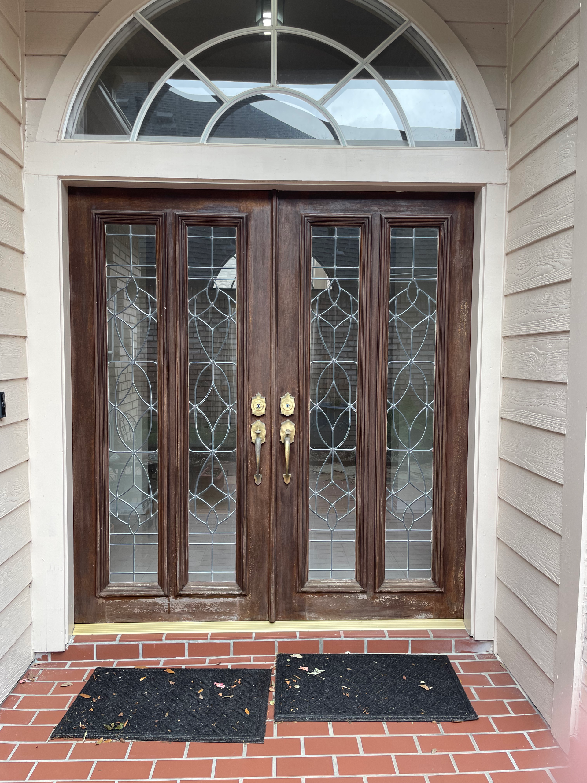 Double wooden doors with glass panels and an arched transom above, set in a brick entryway.