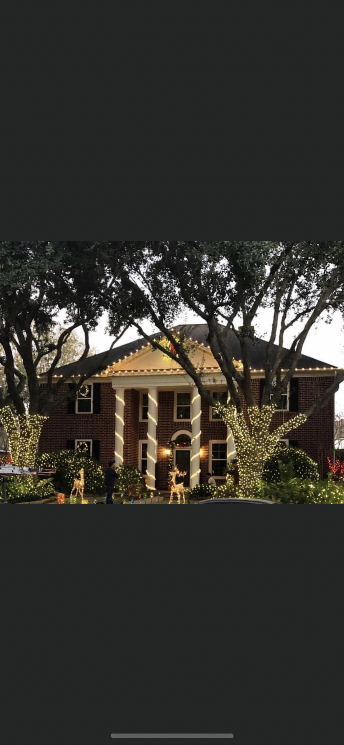A grand brick house with white columns, lit with string lights, framed by trees.