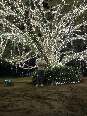Man standing in front of a tree covered in white lights at night.