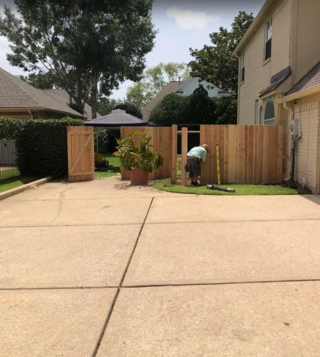 Man building a wooden fence in a residential yard. A driveway is in the foreground.