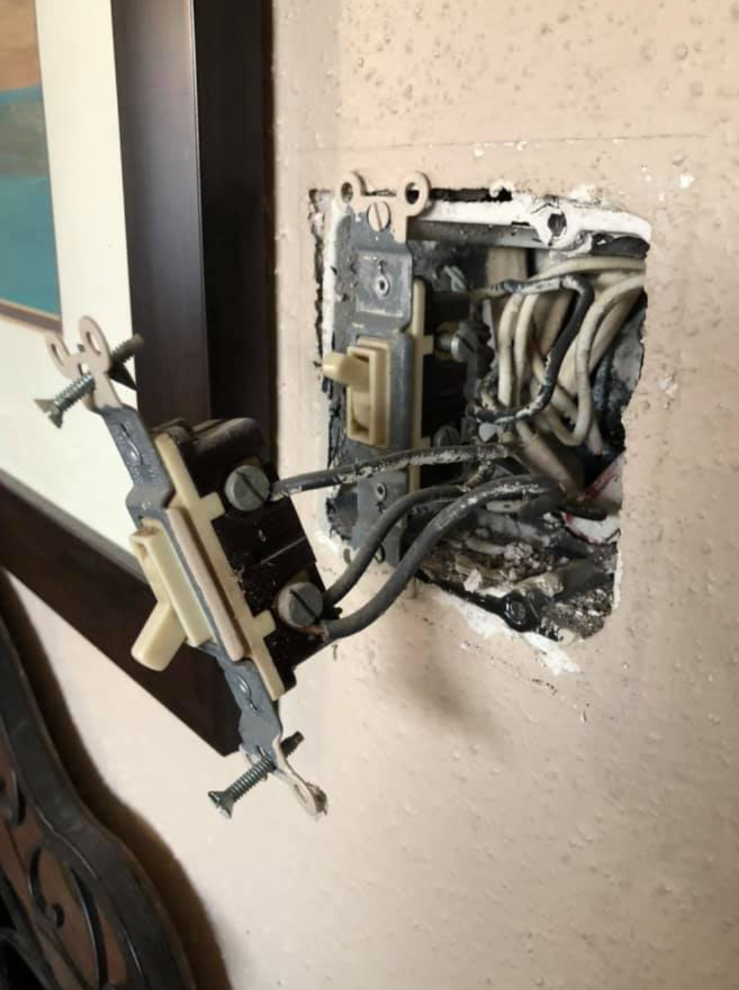 Exposed light switch with wires, detached from wall, showing charring and damage.
