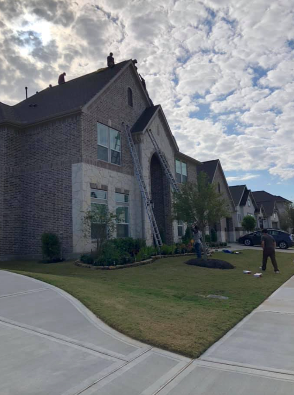 Workers on ladders repairing a brick house roof on a sunny day.