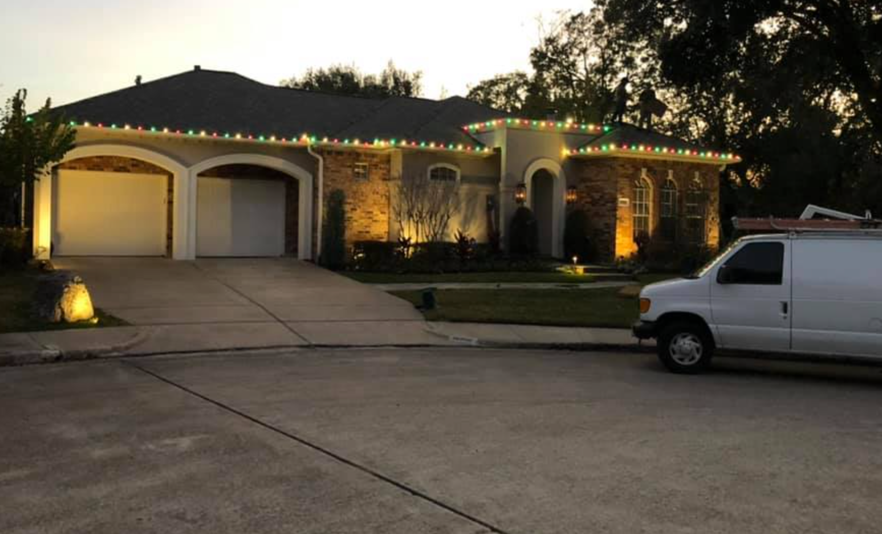 House with Christmas lights, lit up at dusk, white van parked in driveway.