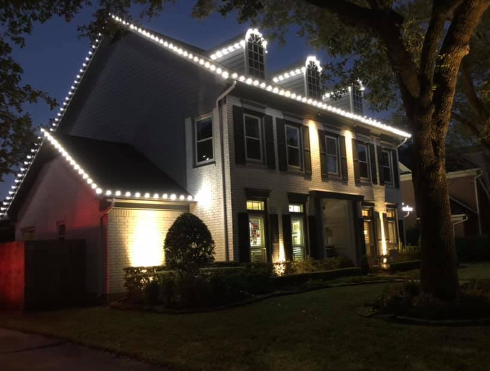 House at night with white Christmas lights lining the roof and windows.