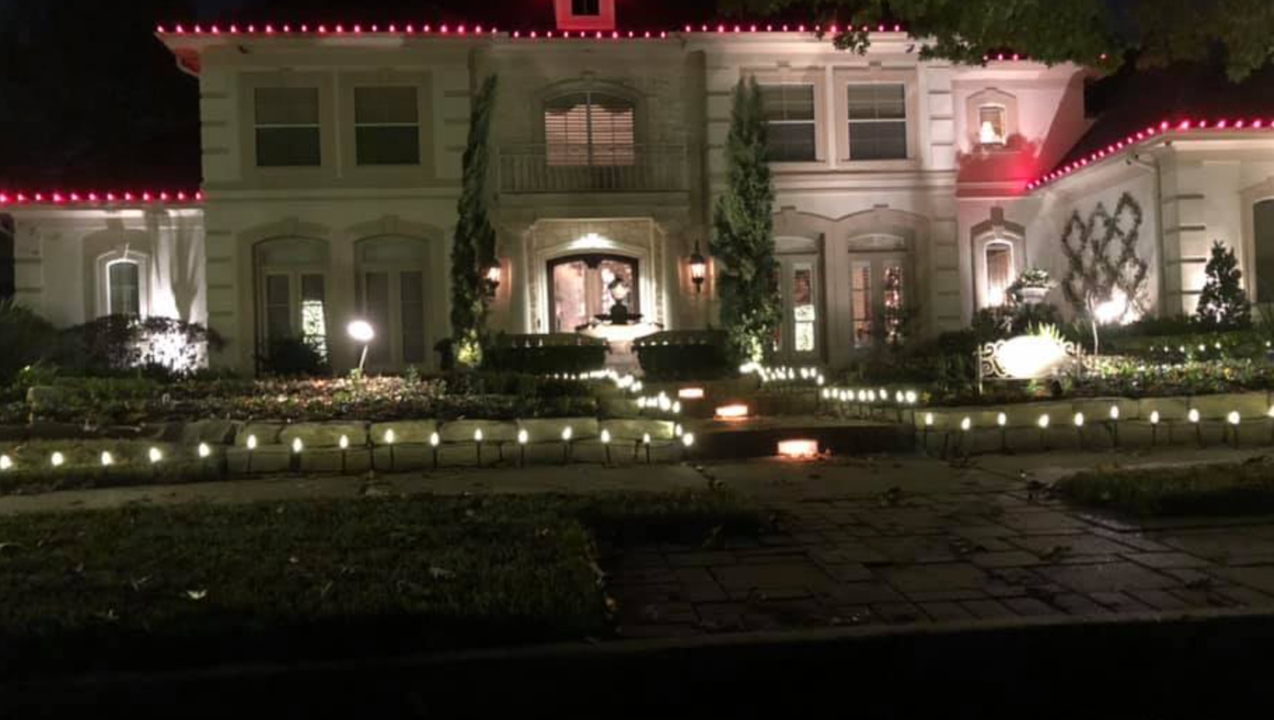Festive house at night, illuminated with red lights along the roof and white lights outlining the yard.