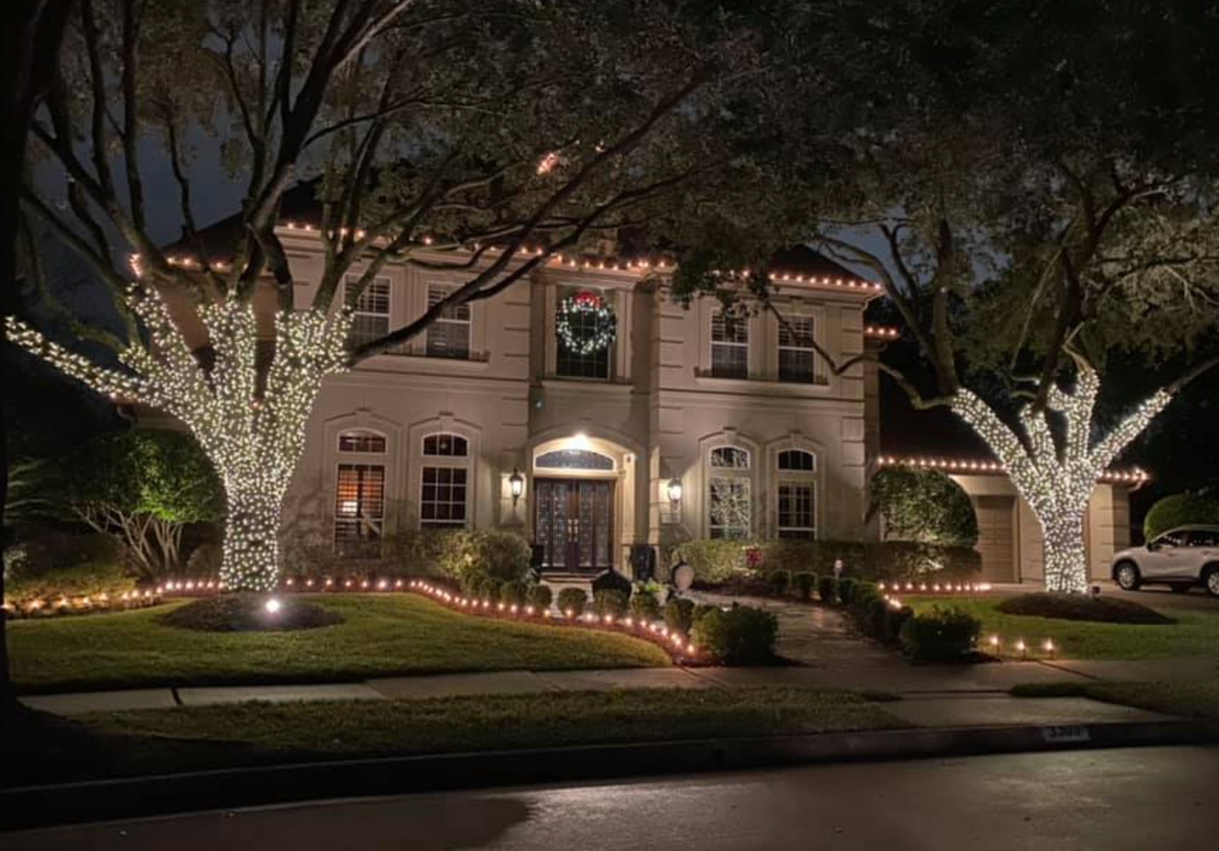 Lit-up house and trees with white Christmas lights at night.