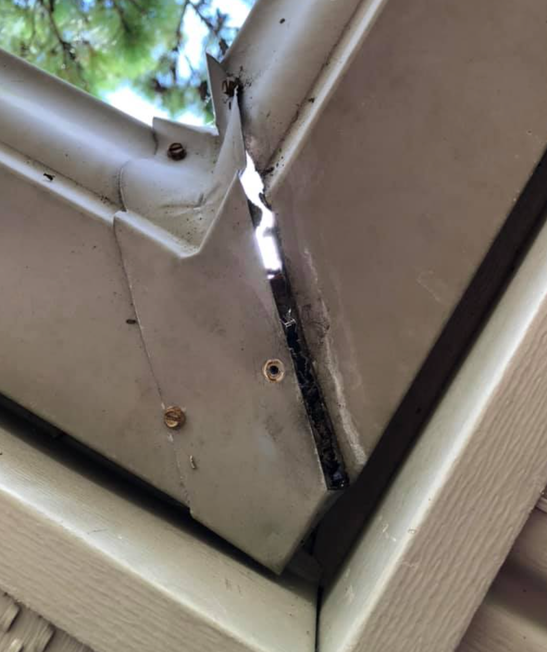 Beige gutter corner, split open with dark debris visible.