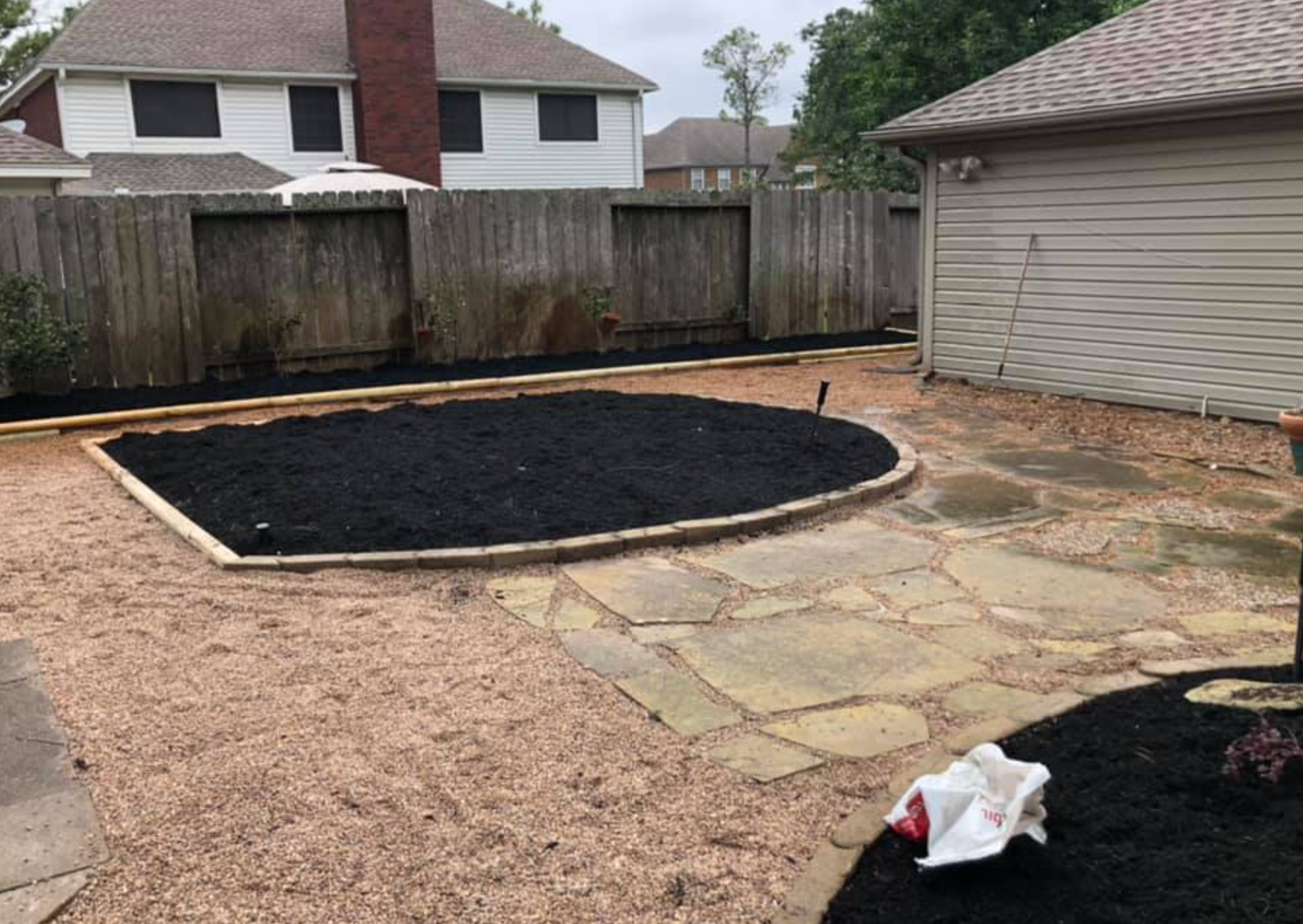 Backyard with mulch bed, flagstone path, and wood fence.