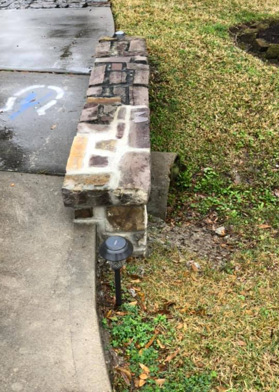 Brick pillar next to a sidewalk and grass, with a low-voltage landscape light in front.