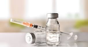 Syringe and two vials with clear liquid; medical setting.