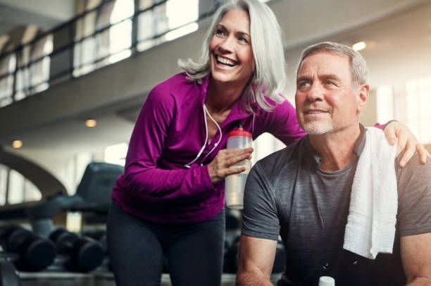 Woman in purple jacket smiling, arm around man in gym setting.