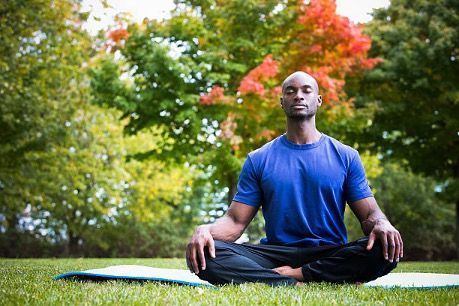 A man is sitting on a yoga mat in a park.