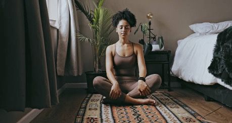 a woman is sitting in a lotus position on a rug in a bedroom .