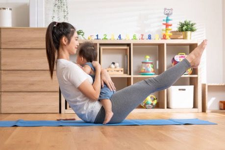 A woman is holding a baby while doing yoga on a yoga mat.