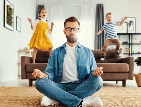 A man is sitting in a lotus position on the floor in a living room.