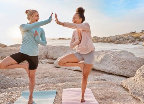 Two women are doing yoga on the beach and giving each other a high five.