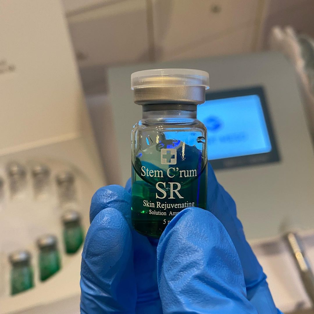 A person wearing blue gloves is holding a bottle of stem c serum sr