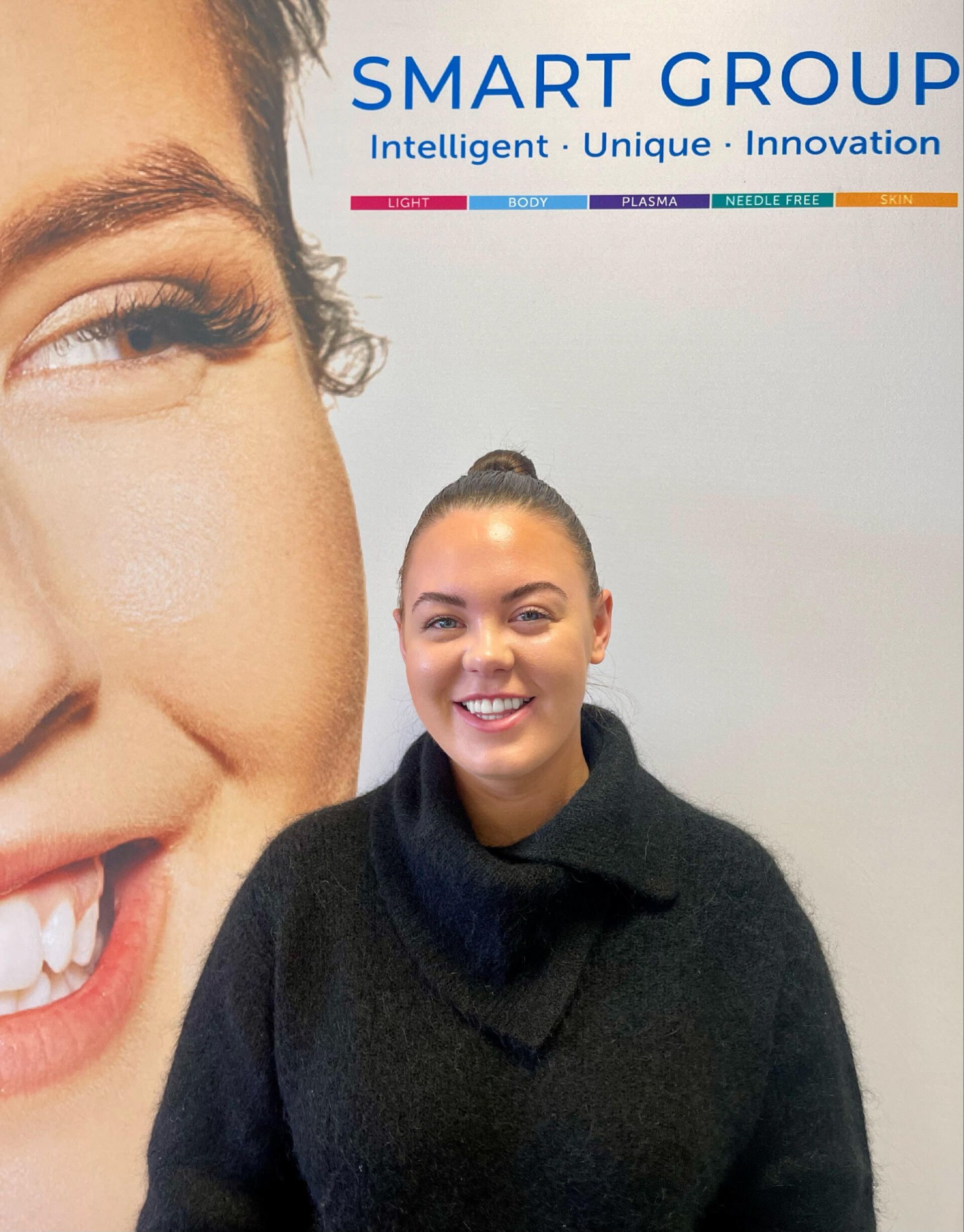 A woman is smiling in front of a smart group poster.