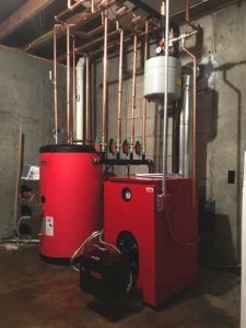 Red heating system components with copper pipes in a basement setting.