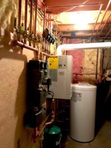 Basement with heating system components, including a water heater, furnace, copper piping, and green tank.