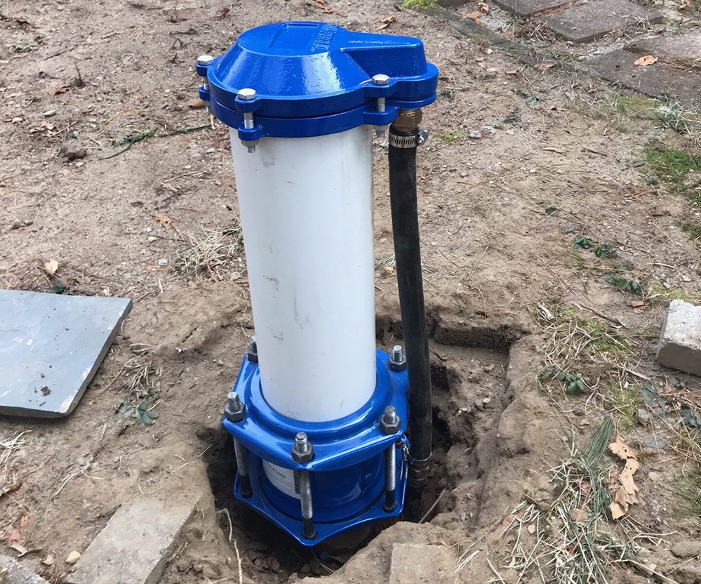 Blue and white wellhead in dirt; a black hose emerges.