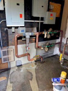 Copper pipes, electrical panels, and a wet floor in a utility room.