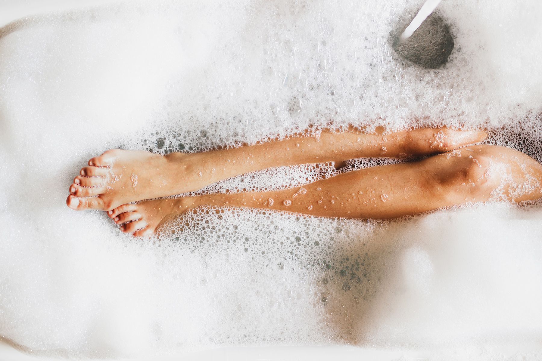 Woman's legs and feet in a bathtub filled with bubbly white foam; red nail polish.