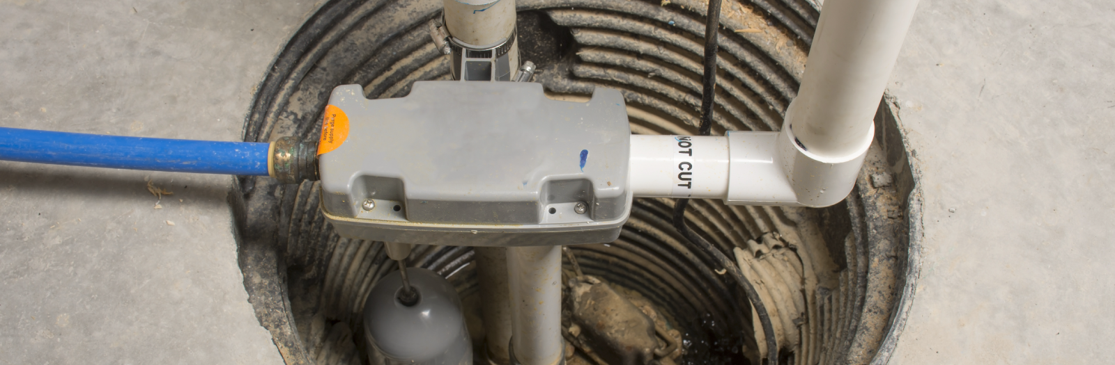 Sump pump basin with blue and white pipes. The basin is in a concrete floor.