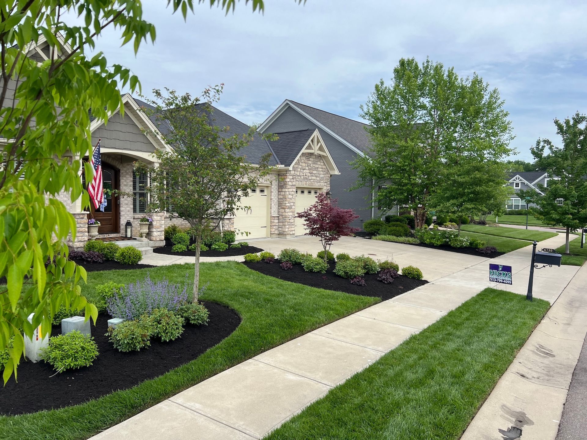 Suburban house with well-manicured lawn, landscaped beds, and a sidewalk.